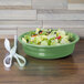 A green Fiesta china bowl filled with salad on a table.