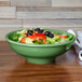 A green Fiesta pedestal serving bowl filled with salad on a table.