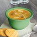 A bowl of bouillon soup with a green rim on a napkin with crackers and a spoon.