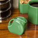 A green Fiesta mini disc creamer pitcher on a wood surface.