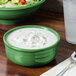A green Fiesta china chowder bowl with white food inside on a table with a bowl of salad.