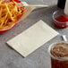 A basket of french fries next to a Choice ecru 2-ply paper napkin and a drink.