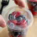A clear plastic flat lid without a straw slot on a cup filled with blueberries and raspberries.