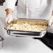 A chef holding a Vollrath stainless steel food pan filled with food.