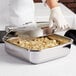 A person in gloves holding a Vollrath stainless steel pan of food over a counter.