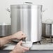 A person using a faucet to fill a large silver stock pot with water.
