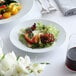 A white 10 Strawberry Street porcelain plate with salad and fruit on a table.