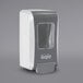 A white and grey GOJO manual soap dispenser with a plastic window.