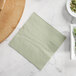 A soft sage green Hoffmaster beverage napkin on a table with a bowl of beans and peanuts.