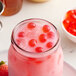A glass jar filled with pink liquid and red berries.