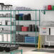 A school kitchen with a green metal Regency wire shelving kit holding various items.