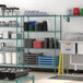 A green metal Regency wire shelving unit on a kitchen counter with various items on the shelves.