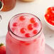 A glass jar filled with pink liquid and Bossen Pure25 Strawberry Bursting Boba with red berries.