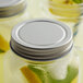 An Arcoroc silver metal drinking jar with a lid filled with lemonade.