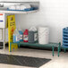 A Regency green epoxy wire shelf kit in a kitchen with a white container of blue liquid on a shelf above a sink.