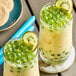 Two glasses of green bubble tea with kiwi slices in them.