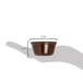 A hand holding a Carlisle brown melamine ramekin with a measuring tape.