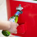 A hand holding a green bottle of beer and placing it into a red Choice Beverage Cooler Cart.