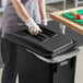 A person wearing gloves putting a black trash can into a school kitchen.