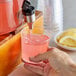 A person pouring Narvon Pink Lemonade concentrate into a glass of water.