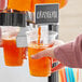 A person pouring Narvon orange beverage into a plastic cup.