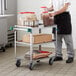 A man standing next to a Regency stainless steel utility cart with containers of brown liquid on it.