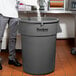 A man standing next to a large grey Continental round trash can pouring water into it.