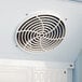 A white circular fan cover mounted inside a commercial refrigerator.