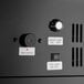 A close-up view of the control panel on a black glass door merchandiser refrigerator, showing temperature and lamp controls.