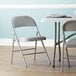 A Lancaster Table & Seating gray vinyl folding chair with a padded seat at a table with a white tablecloth.