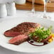 A Warrington Farm Meats New York strip steak on a white plate with green sprouts.