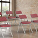 A group of Lancaster Table & Seating burgundy fabric folding chairs with red cushions.