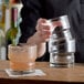 A bartender pouring a drink into a Libbey Newton cocktail glass garnished with rosemary.