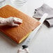 A person's hand using a Mercer Culinary Millennia cake slicer to cut a cake.