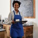 A woman wearing a Royal Blue Choice bib apron holding a tray of coffee cups.