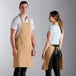 A man and woman wearing Choice khaki bib aprons with pockets.