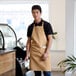 A man wearing a khaki Choice standard bib apron standing in a cafe.