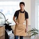 A man wearing a khaki bib apron with pockets standing in front of a counter.