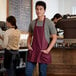 A man wearing a burgundy poly-cotton bib apron with three pockets.