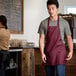 A man wearing a burgundy Choice front of house bib apron.