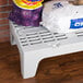 A white plastic bench with bags of food on a Cambro bow tie dunnage rack.