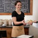 A woman in a black shirt wearing a Choice Khaki standard waist apron with three pockets handing a plate of food to a man.