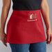 A person wearing a red Choice poly-cotton apron customized with a logo on a counter in a professional kitchen.