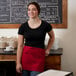 A woman wearing a black shirt and a red Choice apron standing in front of a menu board.