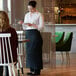 A woman wearing a black Choice standard bistro apron with one pocket standing at a table.