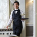 A woman wearing a black and white pinstripe tuxedo apron holding a tray with wine glasses.