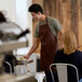 A man in a brown Choice bib apron serving food to a woman.