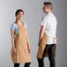 A man and woman wearing tan Choice adjustable bib aprons with pockets.