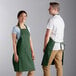 A man and woman wearing Choice hunter green bib aprons.