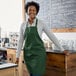 A woman standing in a green Choice bib apron with 2 pockets.